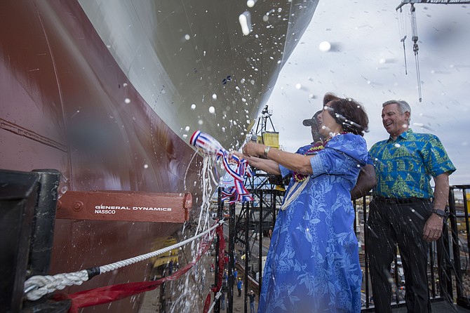 Constance Lau, a member of the Matson shipping company’s board of directors, breaks a bottle over the bow of Matson’s new ship to officially name it Lurline. Looking on is Matson CEO Matthew Cox. Since Matson is a Hawaiian company, both wear Hawaiian print clothing. Photo courtesy of General Dynamics NASSCO.