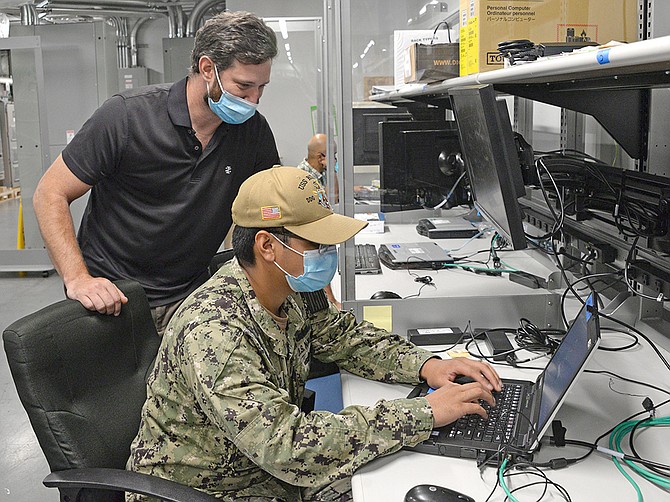In a view from September, Mike Kennedy (left) of Naval Information Warfare Center Pacific instructs Jyro Francisco on loading software at a NIWC Pacific facility. The San Diego command recently extended an IT support contract with SAIC. (Photo courtesy of U.S. Navy)